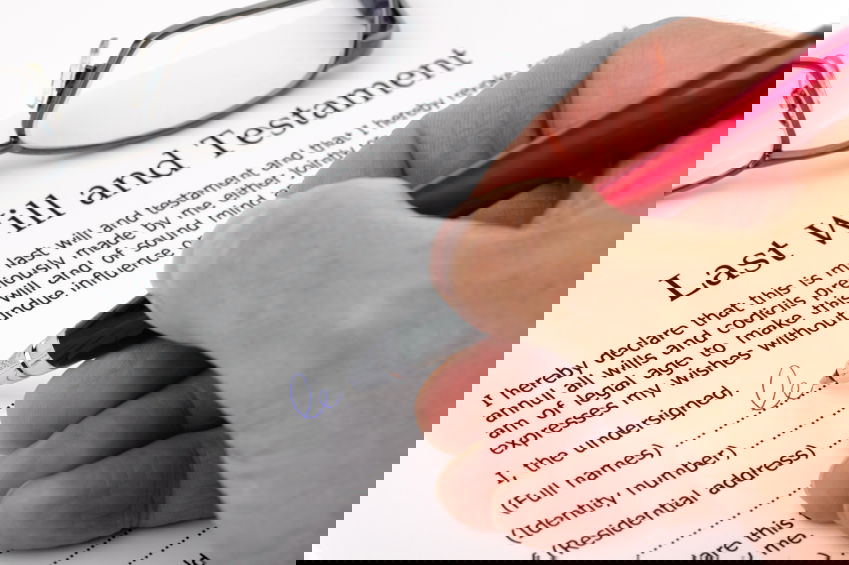 Close-up of a person's hands holding a pen, poised to sign a will, with legal documents and the Turkish flag in the background, symbolizing the act of will writing in Istanbul.